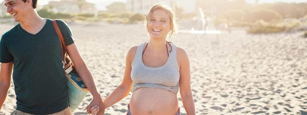 pregnant couple holding hands on beach